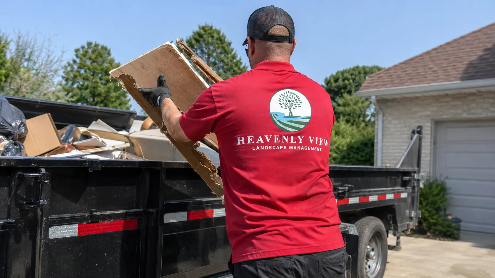 Crew member loading demolition plywood into the black Heavenly View dump trailer